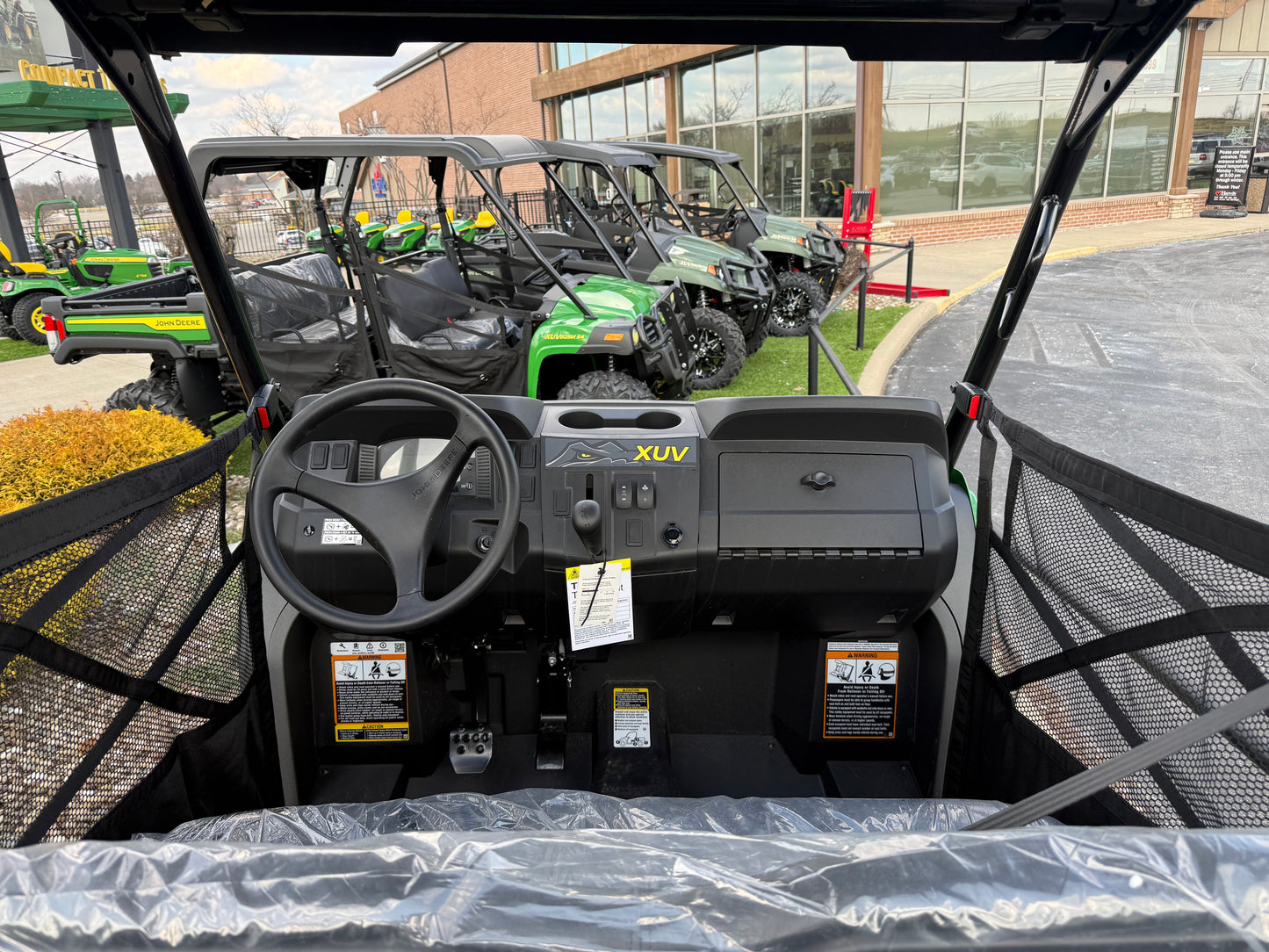 Interior view of a green mid-size utility vehicle dashboard with steering wheel, control panel, and protective mesh sides, displayed outdoors at Hartville Hardware.