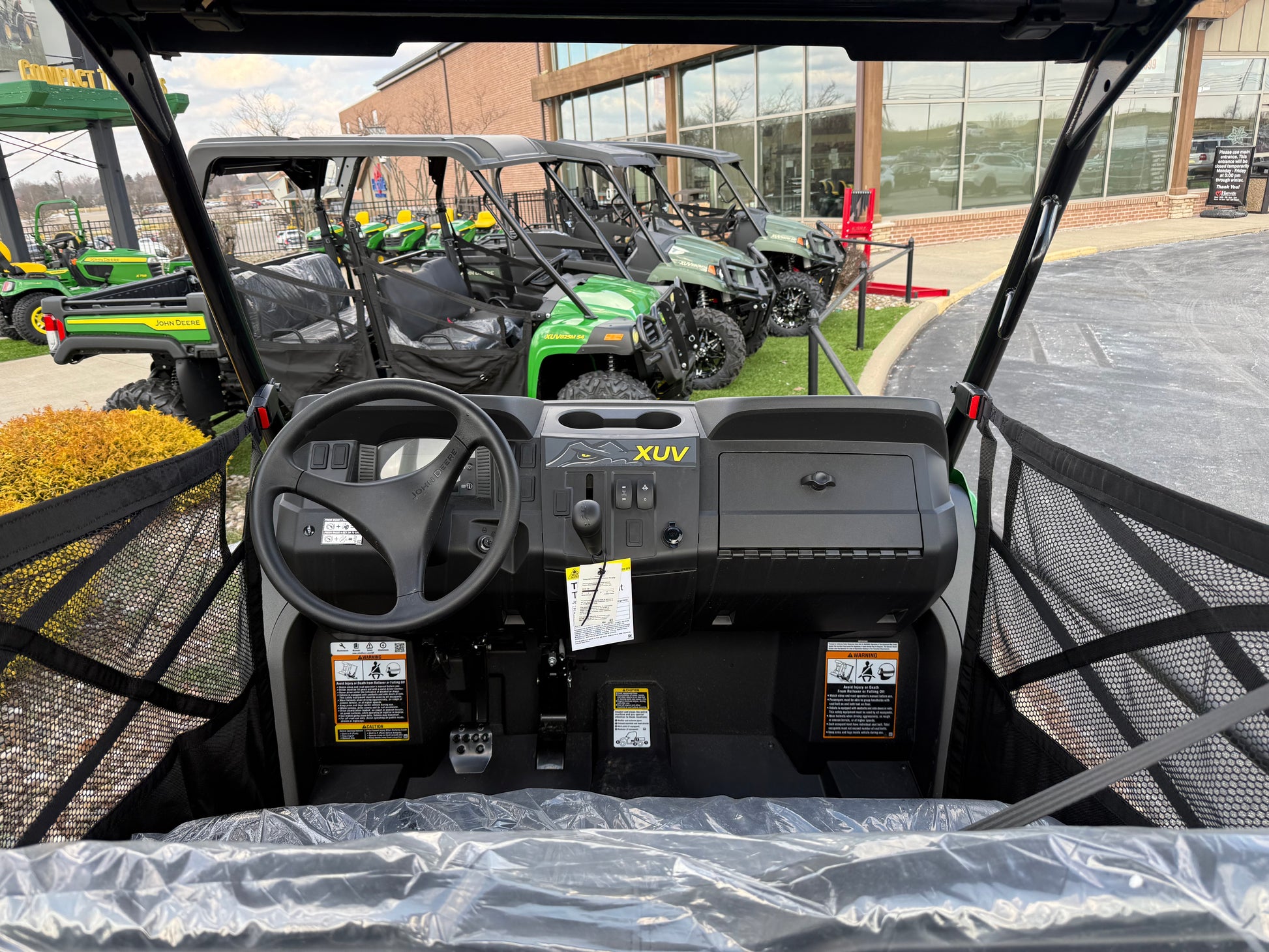 Interior view of a green mid-size utility vehicle dashboard with steering wheel, control panel, and protective mesh sides, displayed outdoors at Hartville Hardware.