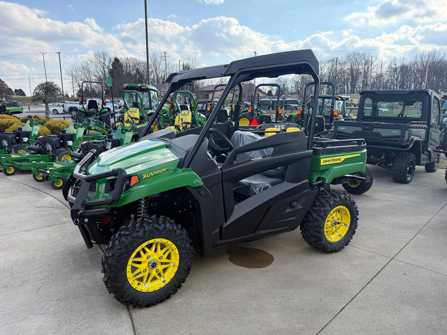 Green and yellow mid-size utility vehicle designed for rugged trails with off-road tires, parked among various John Deere equipment and UTVs collections.