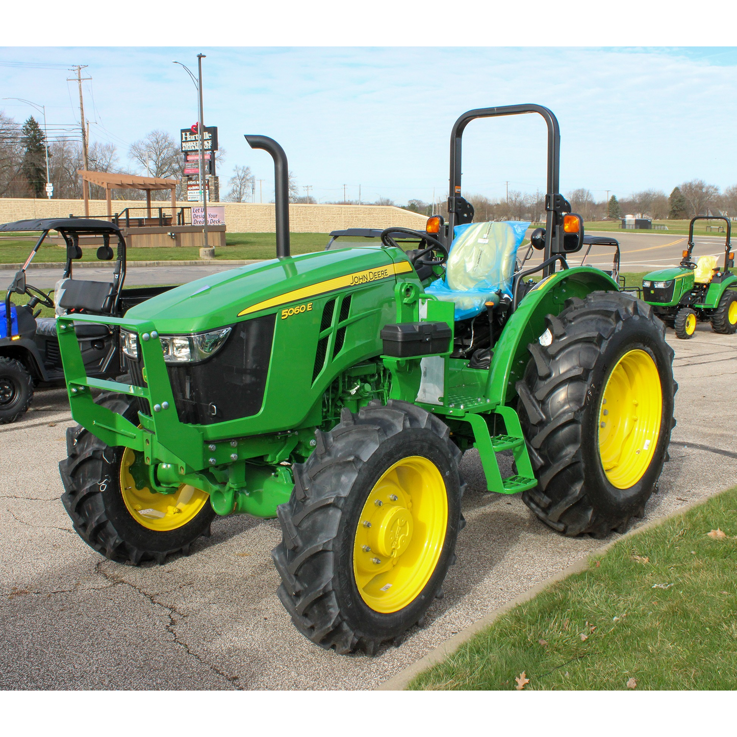 Green John Deere 5060E utility tractor with yellow wheels and protective roll bar displayed outdoors at Hartville Hardware in the John Deere Products section.