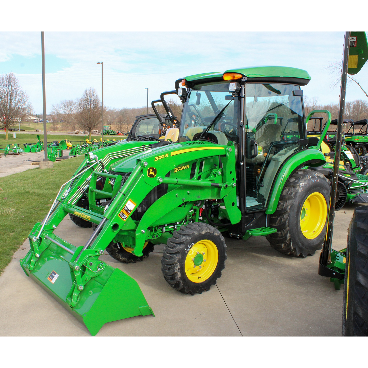 Green John Deere 3039R compact tractor with enclosed ComfortGard cab and front loader attachment displayed outdoors among outdoor power equipment and John Deere parts collections.