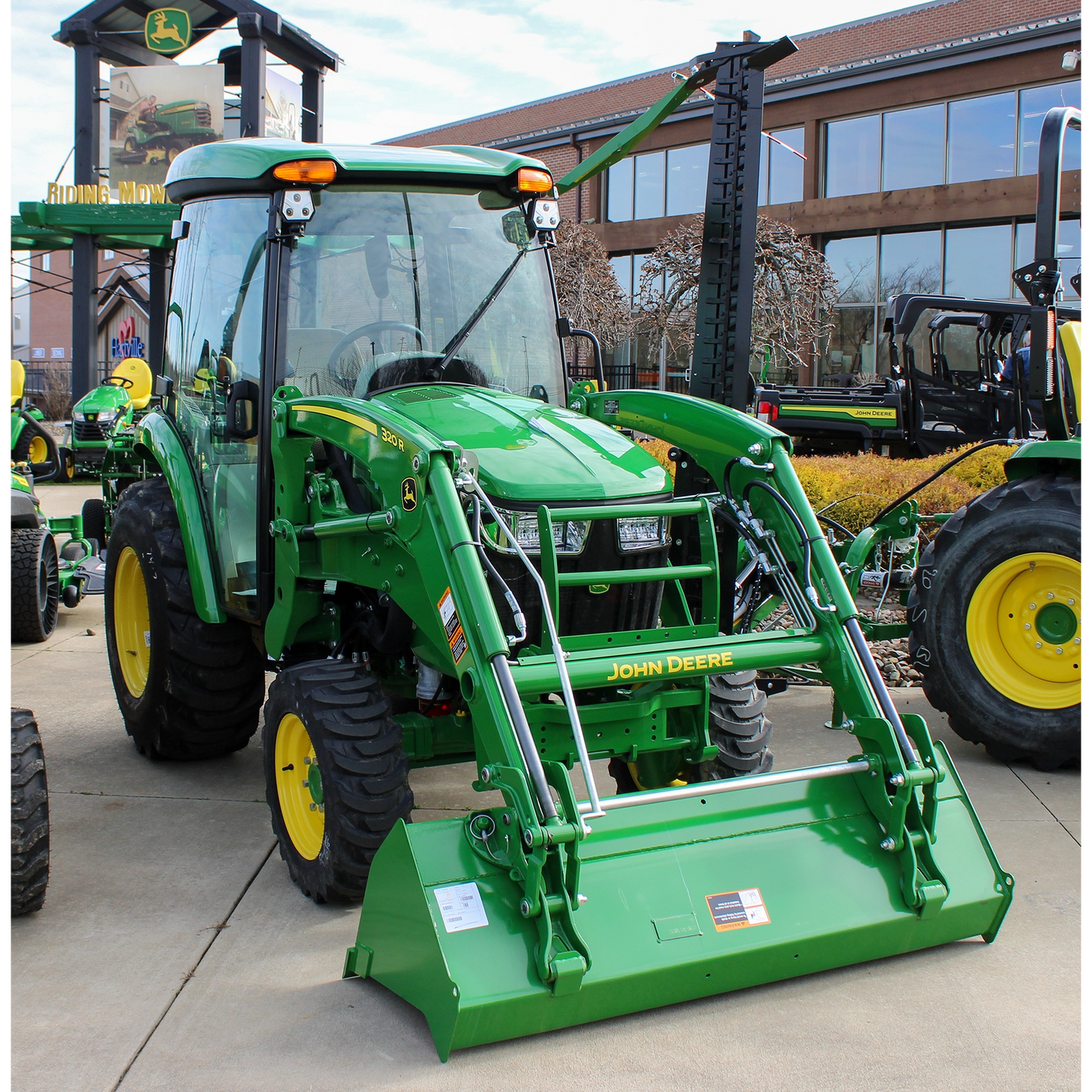 Green John Deere 3039R compact tractor with front loader attachment and enclosed cab, displayed outdoors with other outdoor power equipment and tools.