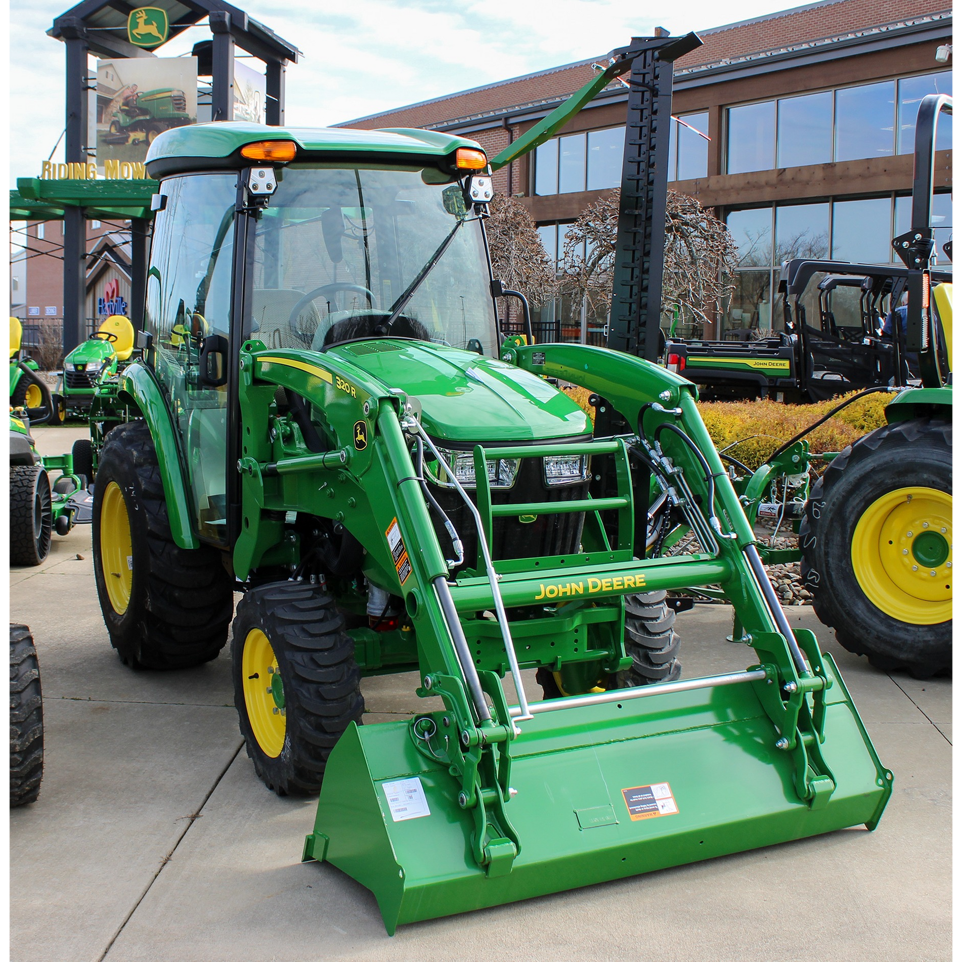 Green John Deere 3039R compact tractor with front loader attachment and enclosed cab, displayed outdoors with other outdoor power equipment and tools.