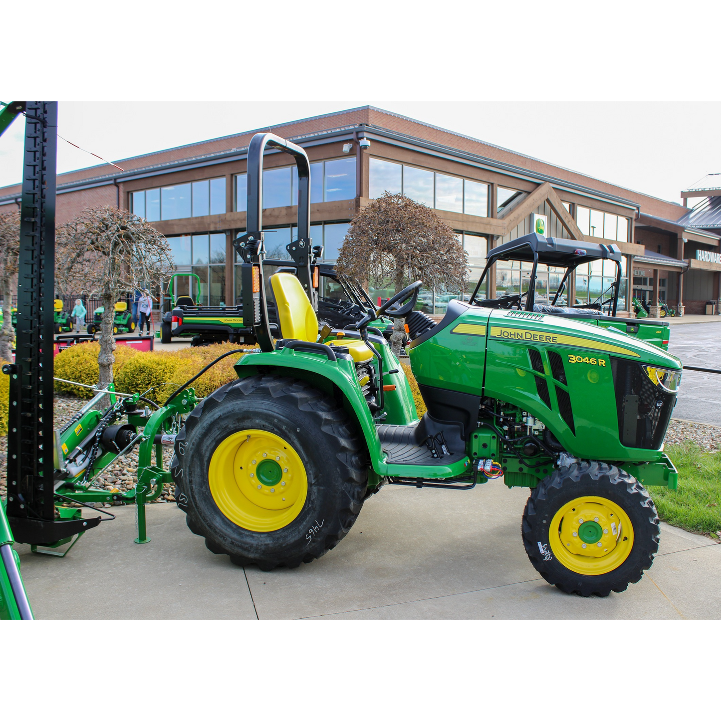 Green John Deere 3046R compact utility tractor with yellow seat and rear agricultural attachment displayed outdoors at Hartville Hardware in the Outdoor Power Equipment section.