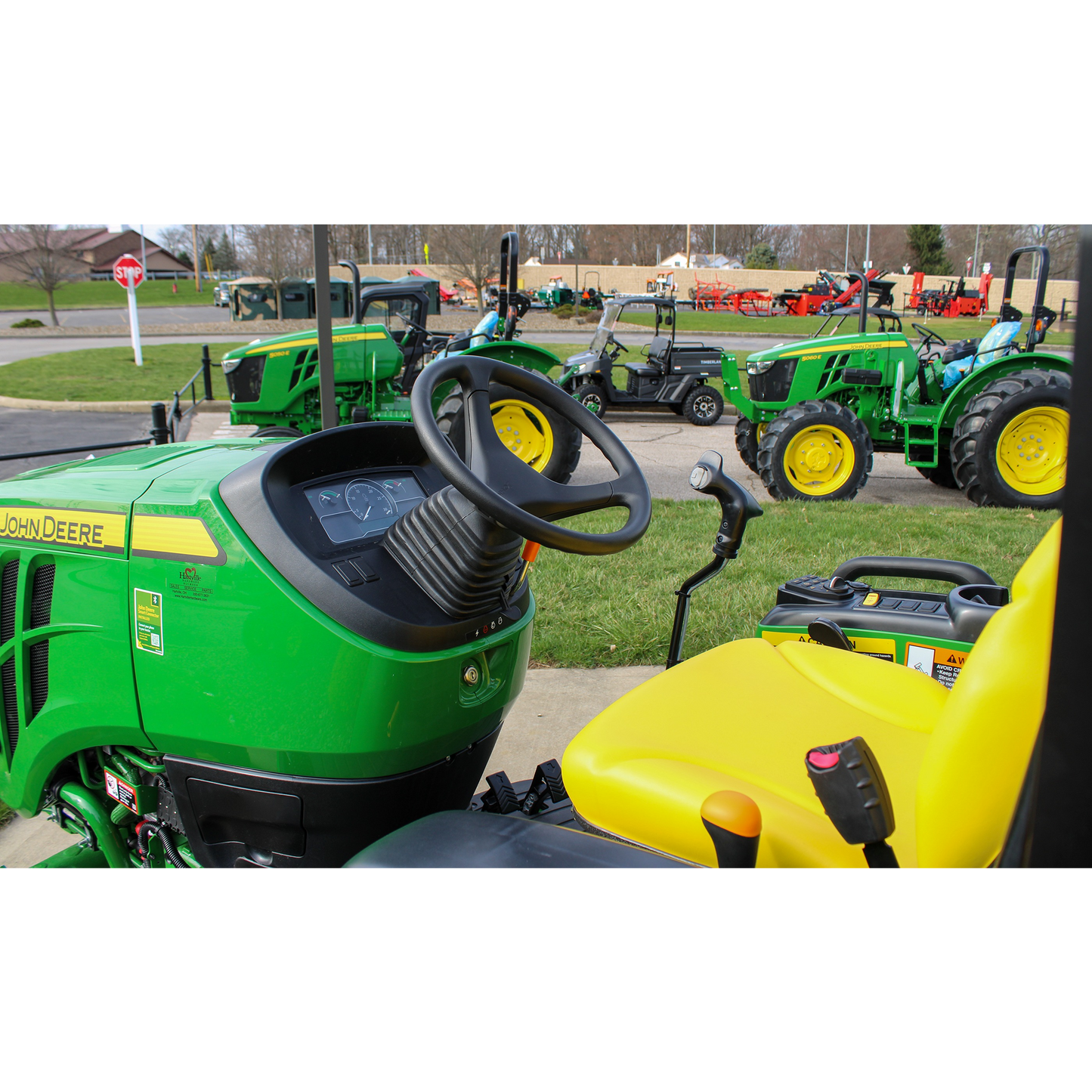 Close-up view of the operator seat and control panel on a green John Deere Custom JD716078 3046R compact utility tractor displayed outdoors among other John Deere equipment at Hartville Hardware in the Outdoor Power Equipment section.