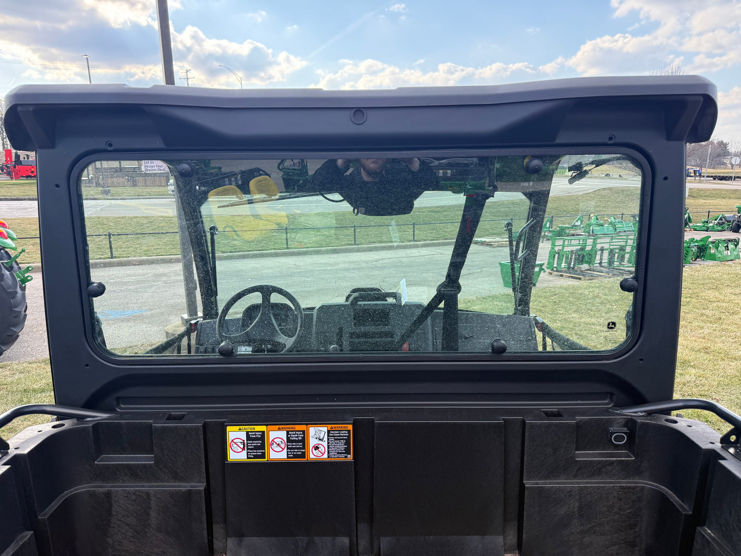 View through the rear window of a John Deere JD718267 Custom XUV 845M crossover utility vehicle showing the interior dashboard and steering wheel at an outdoor equipment lot