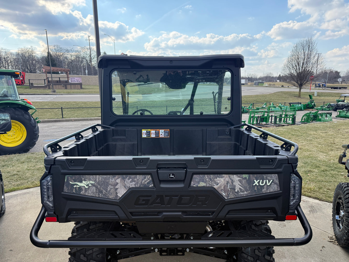 Rear view of a John Deere JD718267 Custom XUV 845M utility vehicle showing the spacious cargo bed and enclosed cab at an outdoor dealership lot