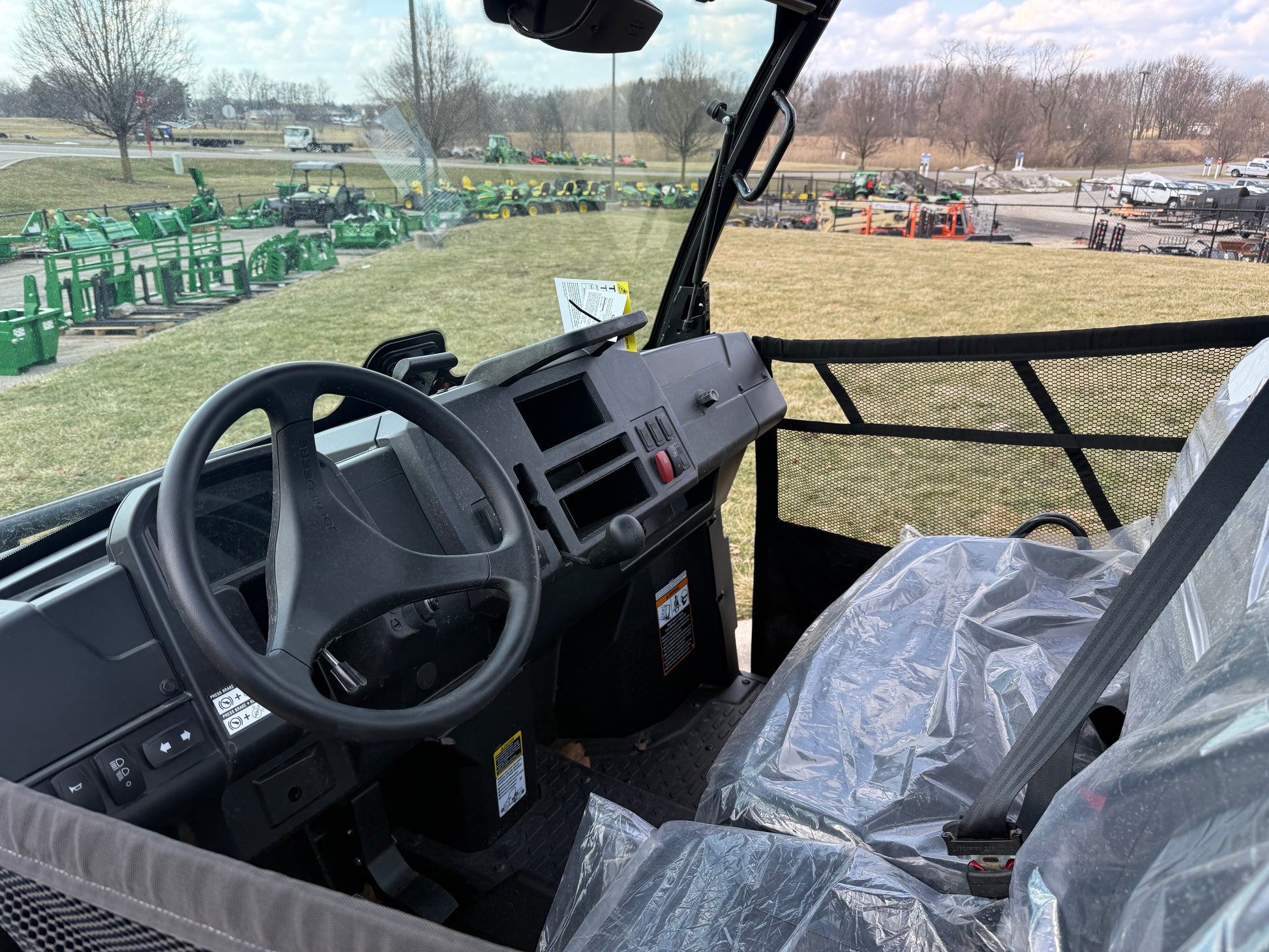 Interior view of a John Deere utility vehicle showing steering wheel, dashboard, and plastic-covered seating at an outdoor dealership lot