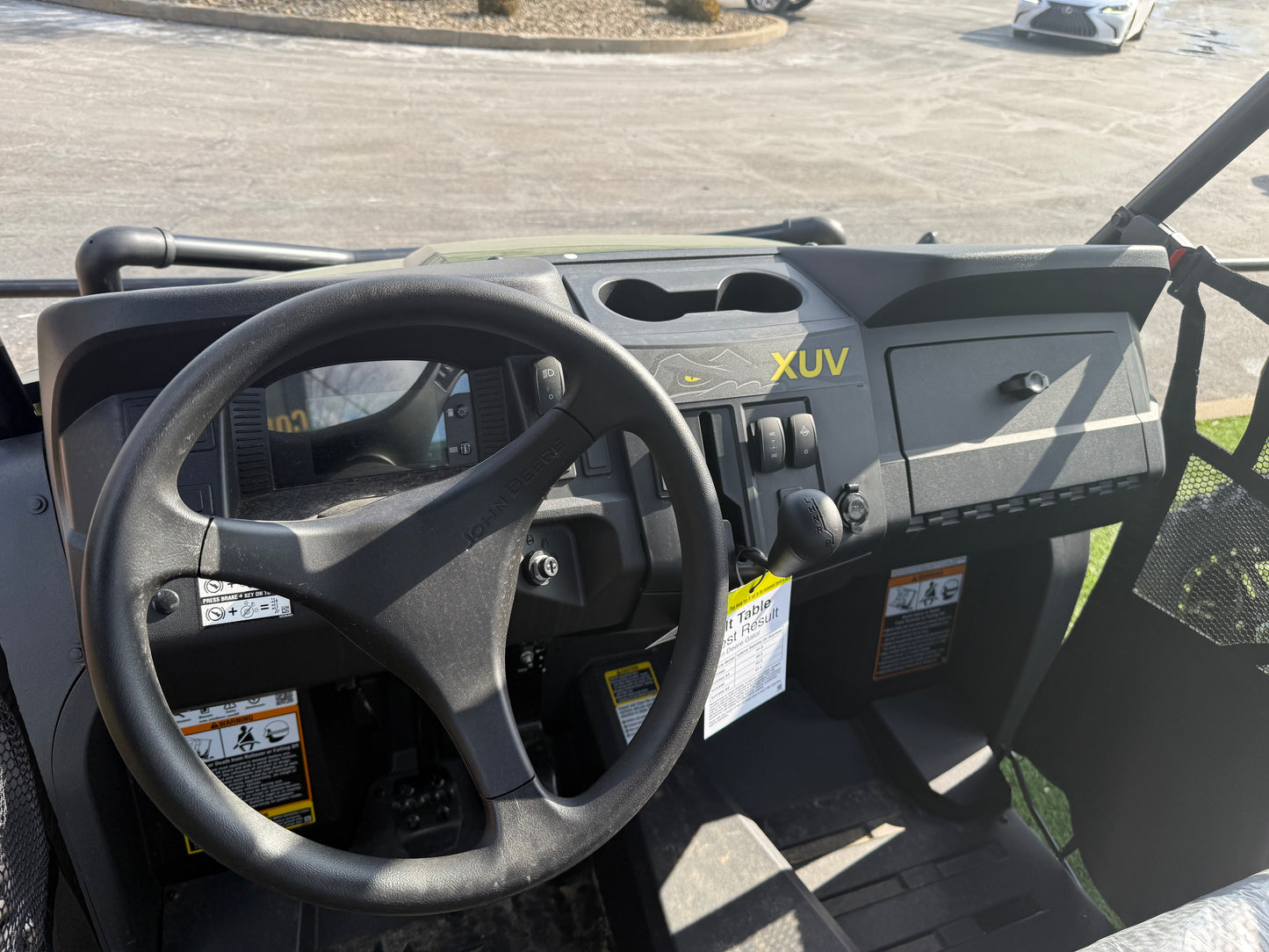 Interior cockpit view of a John Deere 4-seater crossover utility vehicle featuring a steering wheel, dashboard controls, and storage compartments displayed outdoors