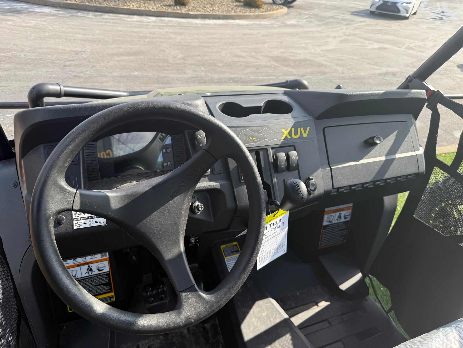 Interior cockpit view of a John Deere 4-seater crossover utility vehicle featuring a steering wheel, dashboard controls, and storage compartments displayed outdoors
