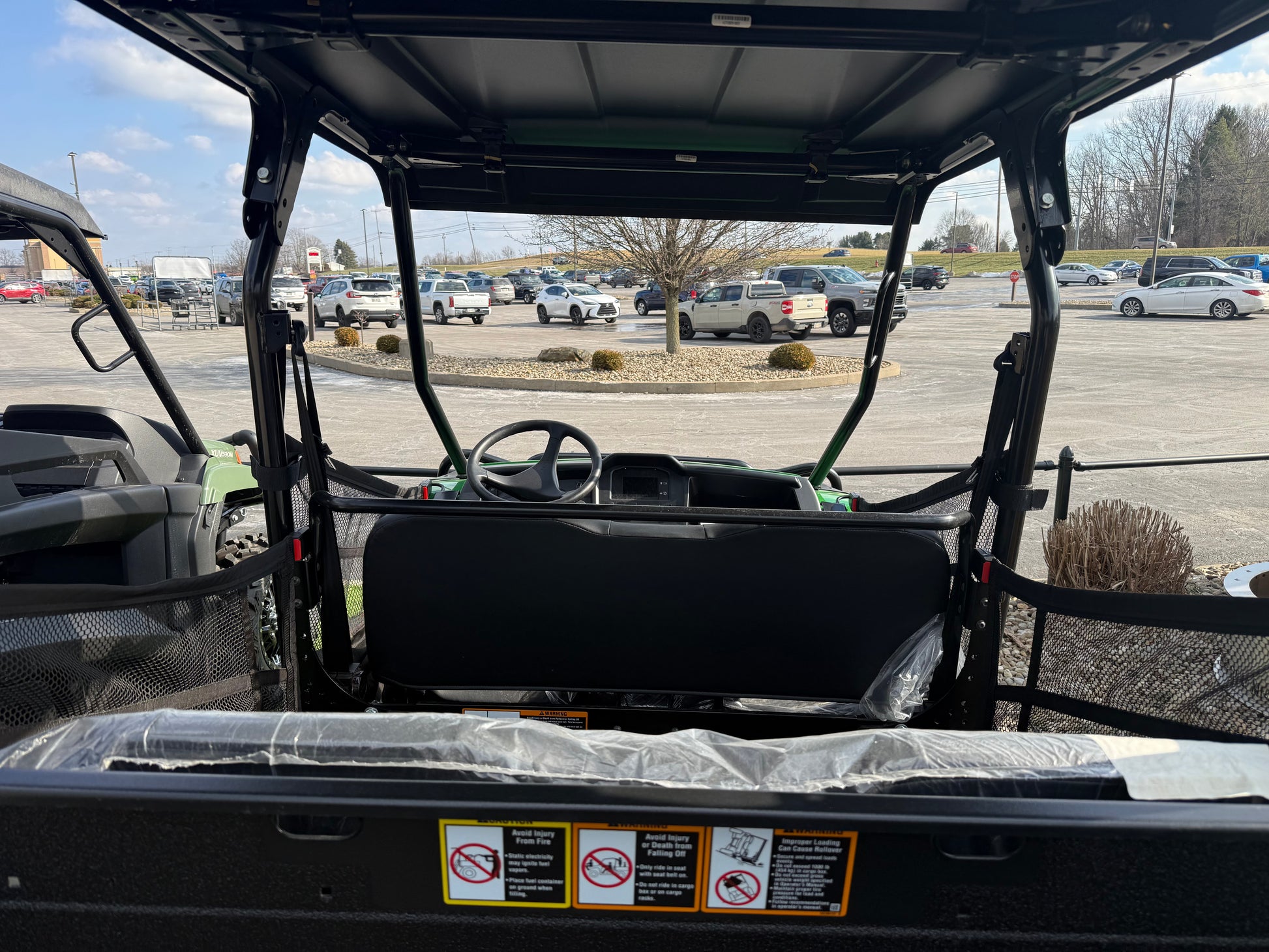 Rear interior view of a John Deere 4-seater crossover utility vehicle showing seats, safety netting, and a protective roof at an outdoor dealership lot.