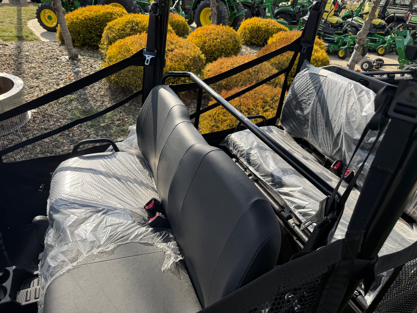 Close-up of the rear passenger seating area in a green John Deere 4-seater crossover utility vehicle with protective safety netting at an outdoor dealership lot.