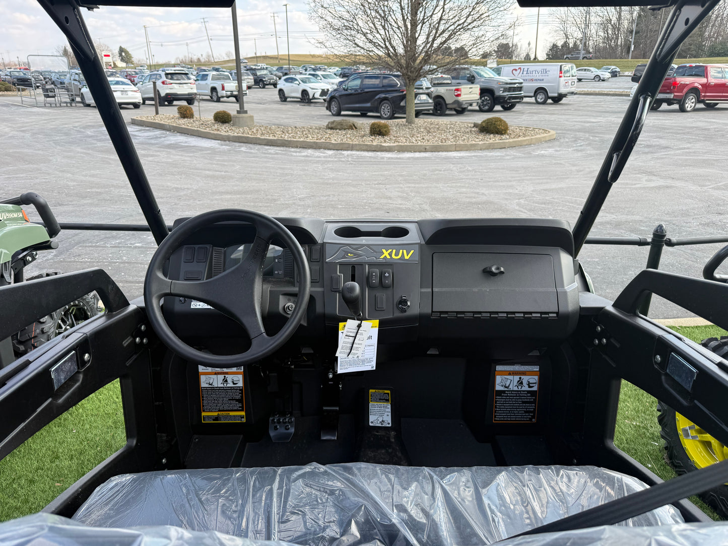 Interior cockpit of a John Deere mid-size crossover utility vehicle featuring steering wheel, dashboard controls, and protective roll cage, displayed outdoors.