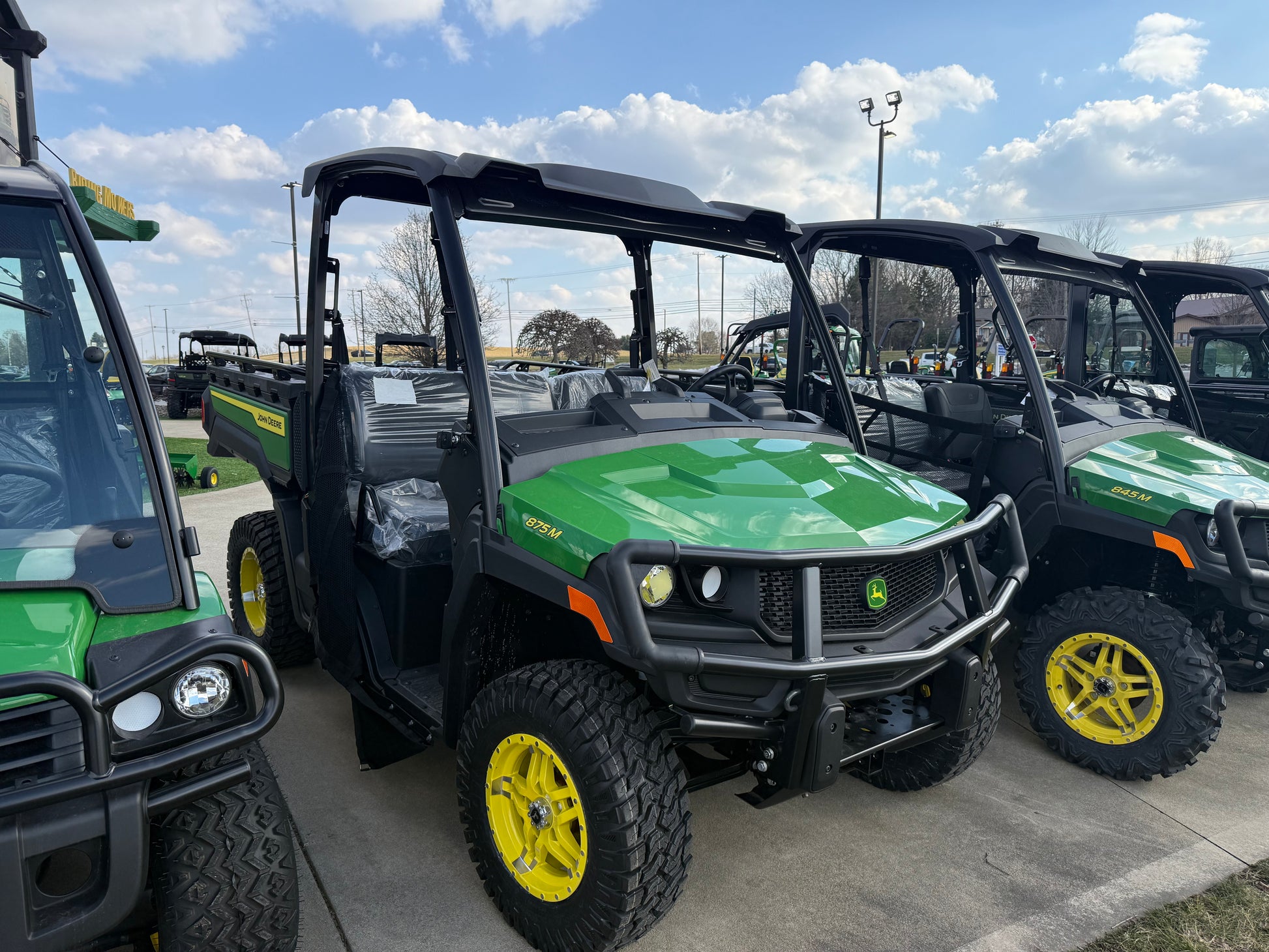 Green diesel crossover utility vehicle with yellow wheels and protective front grille parked alongside similar utility vehicles at outdoor dealership lot