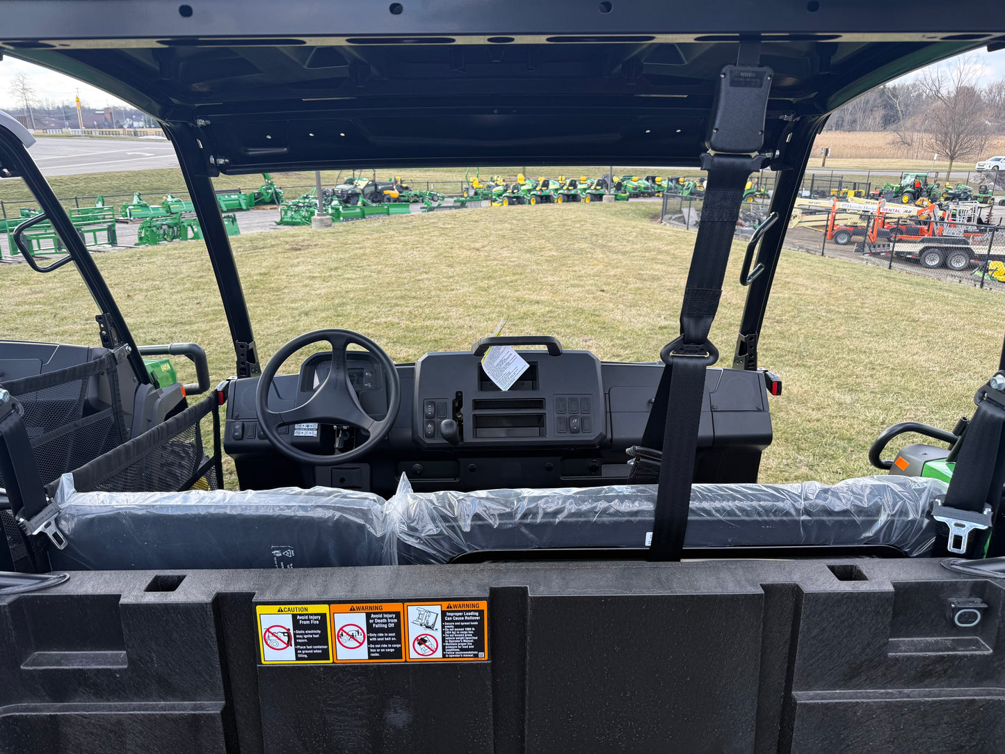 View of the dashboard and steering wheel inside a John Deere diesel crossover utility vehicle with protective seat covers, displayed outdoors among other equipment in a dealership lot