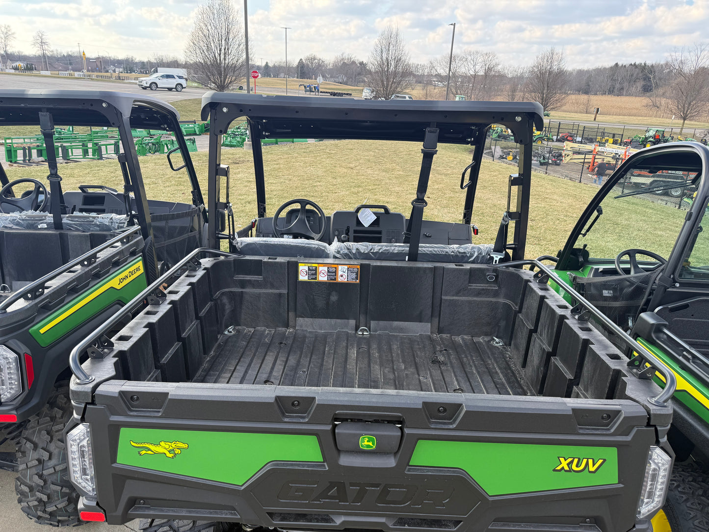 Open cargo bed view of a green John Deere XUV utility vehicle with robust construction, parked outdoors among other UTVs at dealership lot