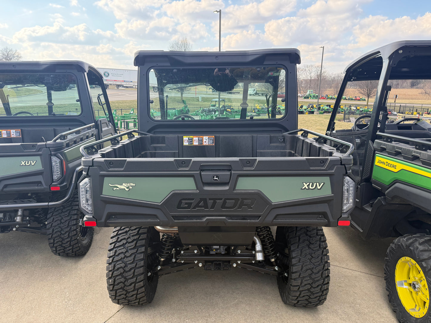 Rear view of a rugged green utility vehicle highlighting a spacious cargo bed and durable off-road tires in an outdoor John Deere equipment lot