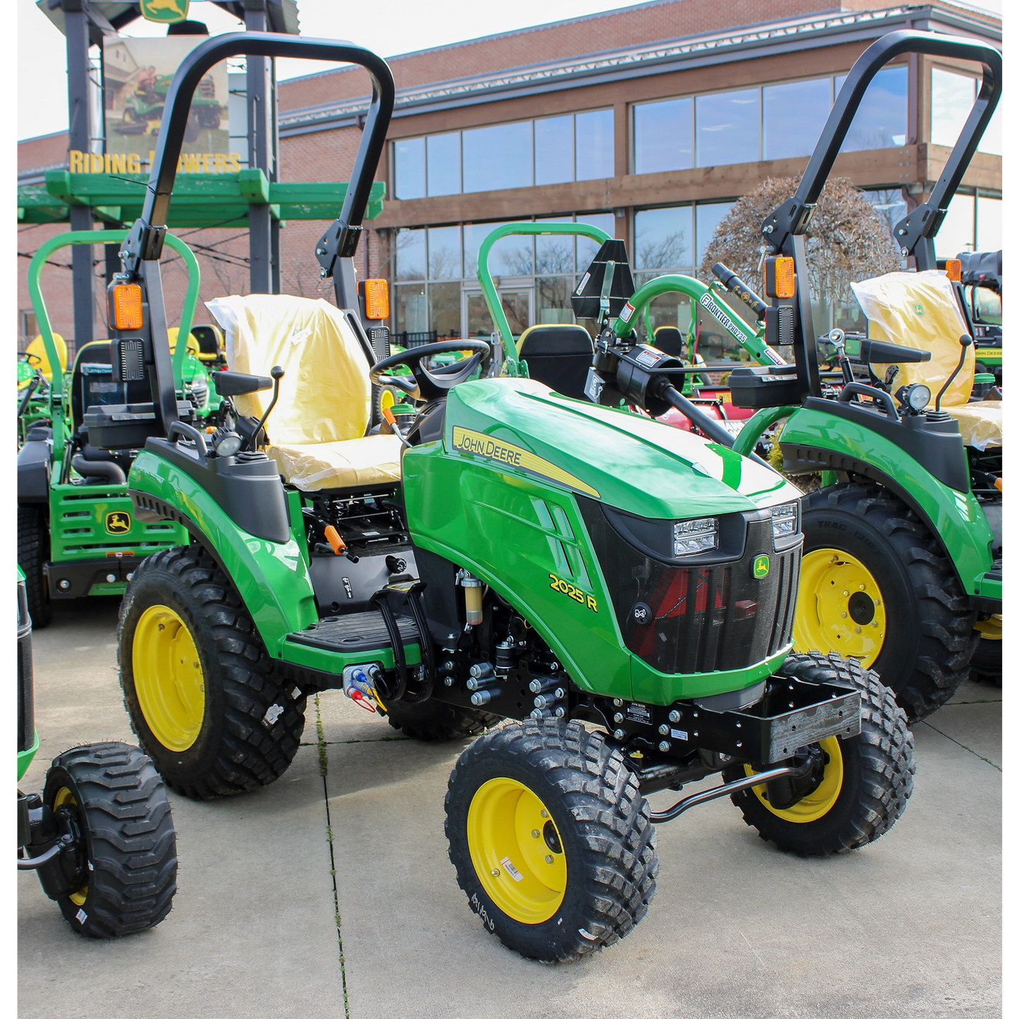Green John Deere 2025R compact tractor with yellow wheels and protective rollover frame, featured in outdoor power equipment and lawn and garden collections.