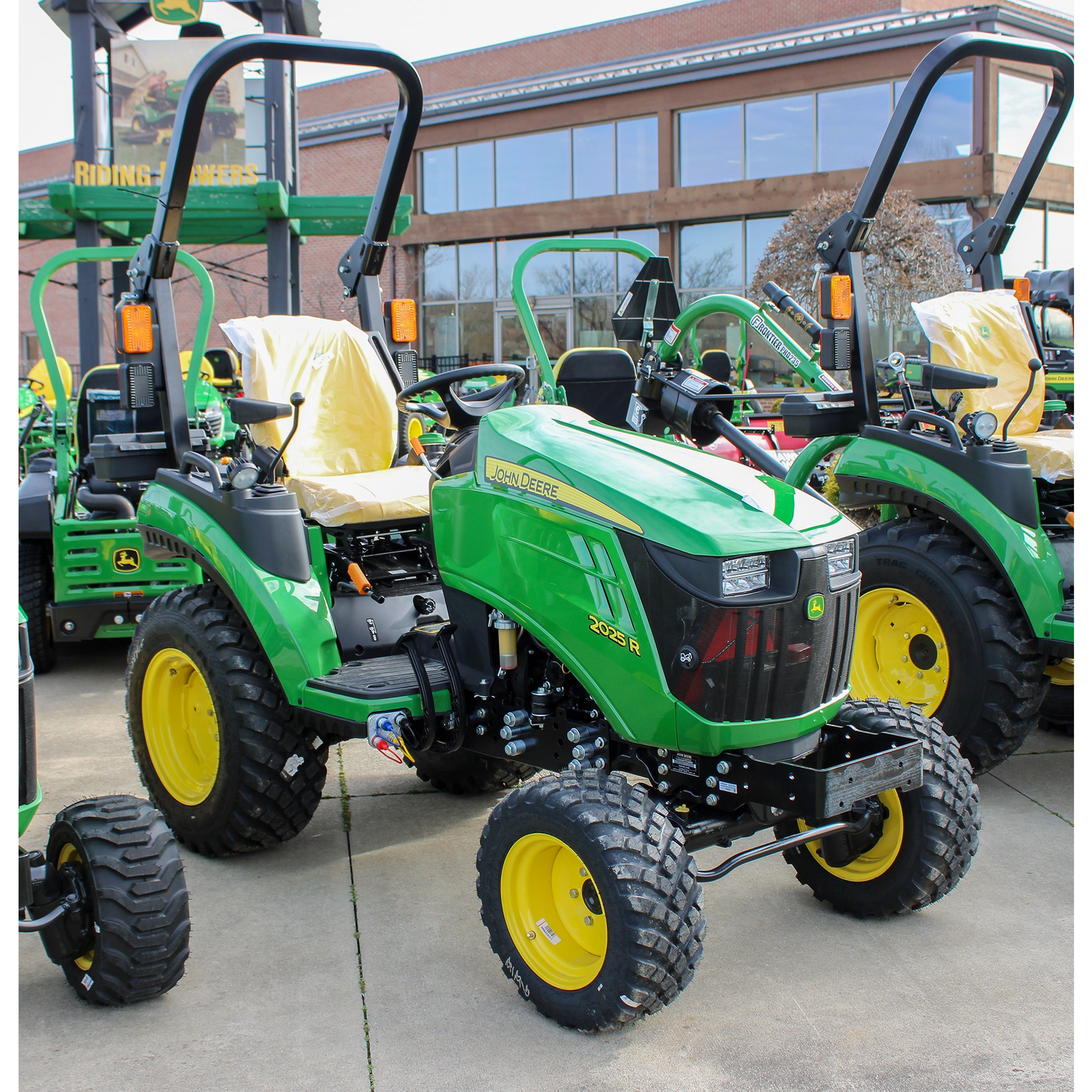 Green John Deere 2025R compact tractor with yellow wheels and protective rollover frame, featured in outdoor power equipment and lawn and garden collections.
