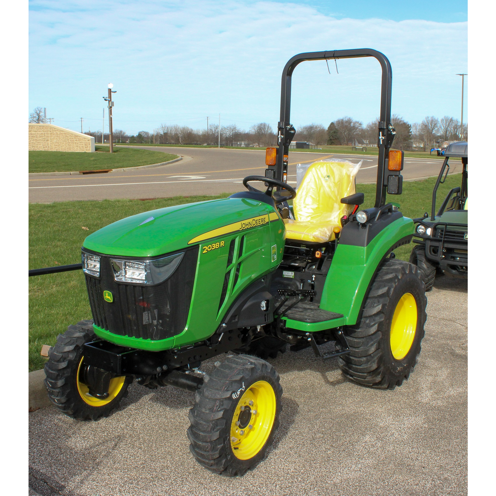 Green John Deere 2038R compact tractor with yellow wheels, rollover protection, and seating covered for protection, featured in outdoor power equipment collections.