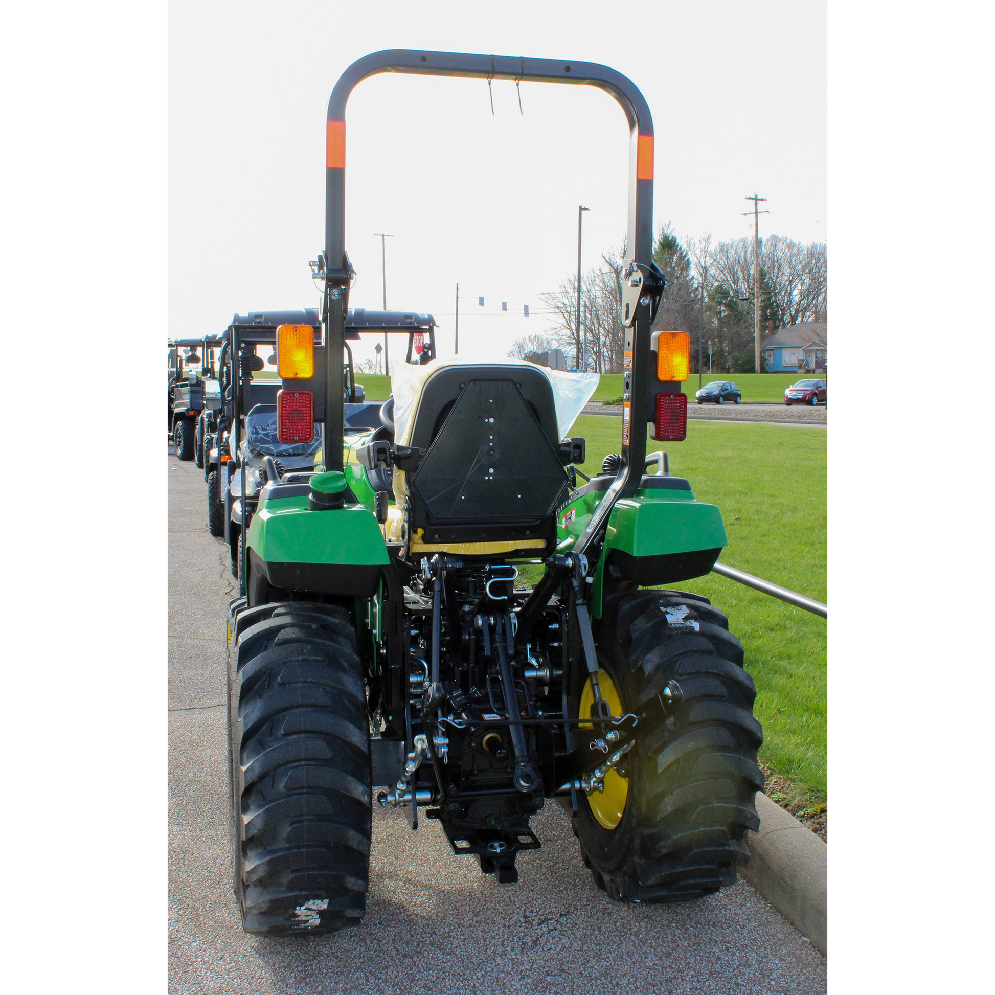 Rear view of a green and yellow John Deere compact tractor with rollover protection, large tread tires, and rear hitch, featured in outdoor power equipment collections.