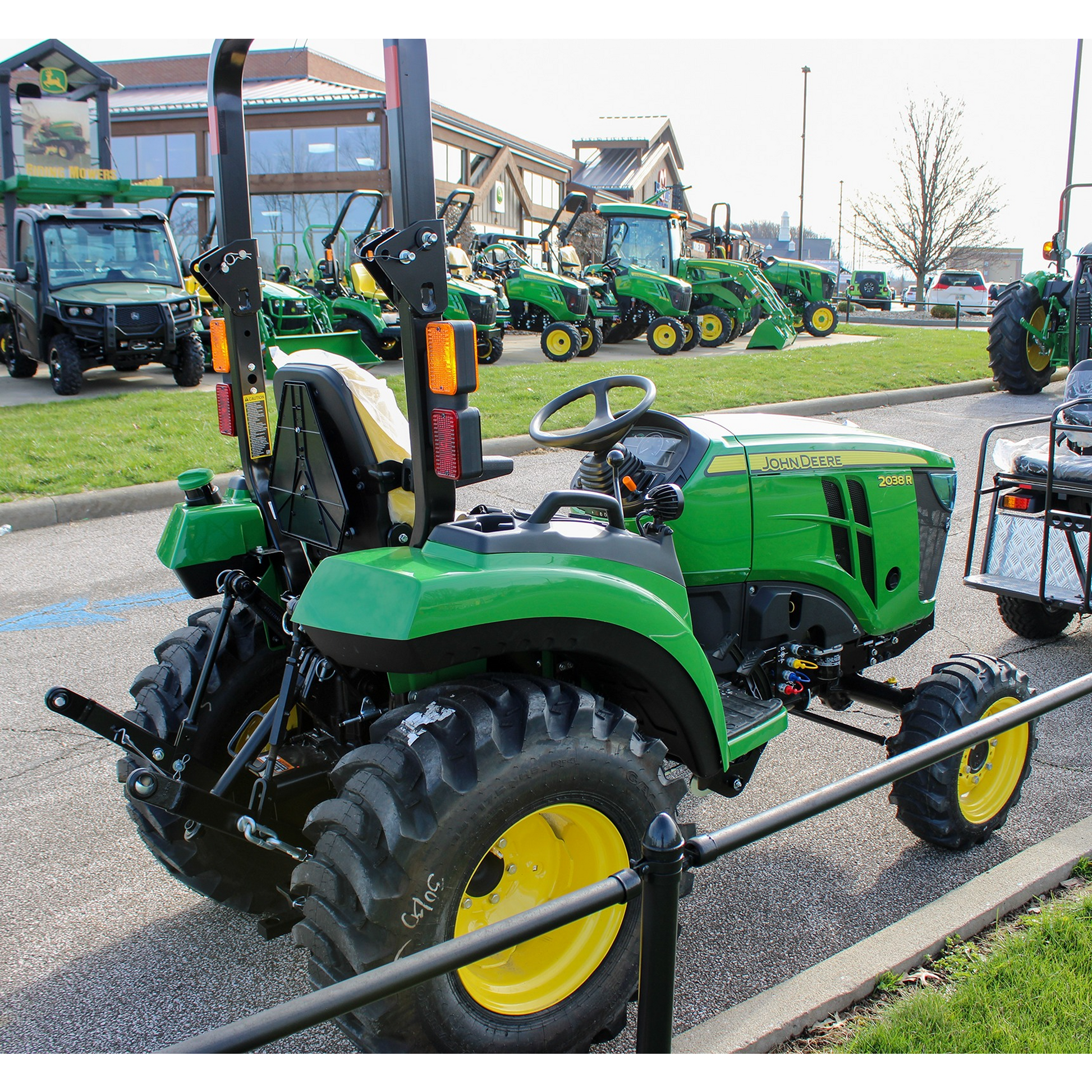 Green compact utility tractor with yellow wheels, rollover protection, and rugged tires displayed outdoors in a John Deere equipment and outdoor power tools collection.