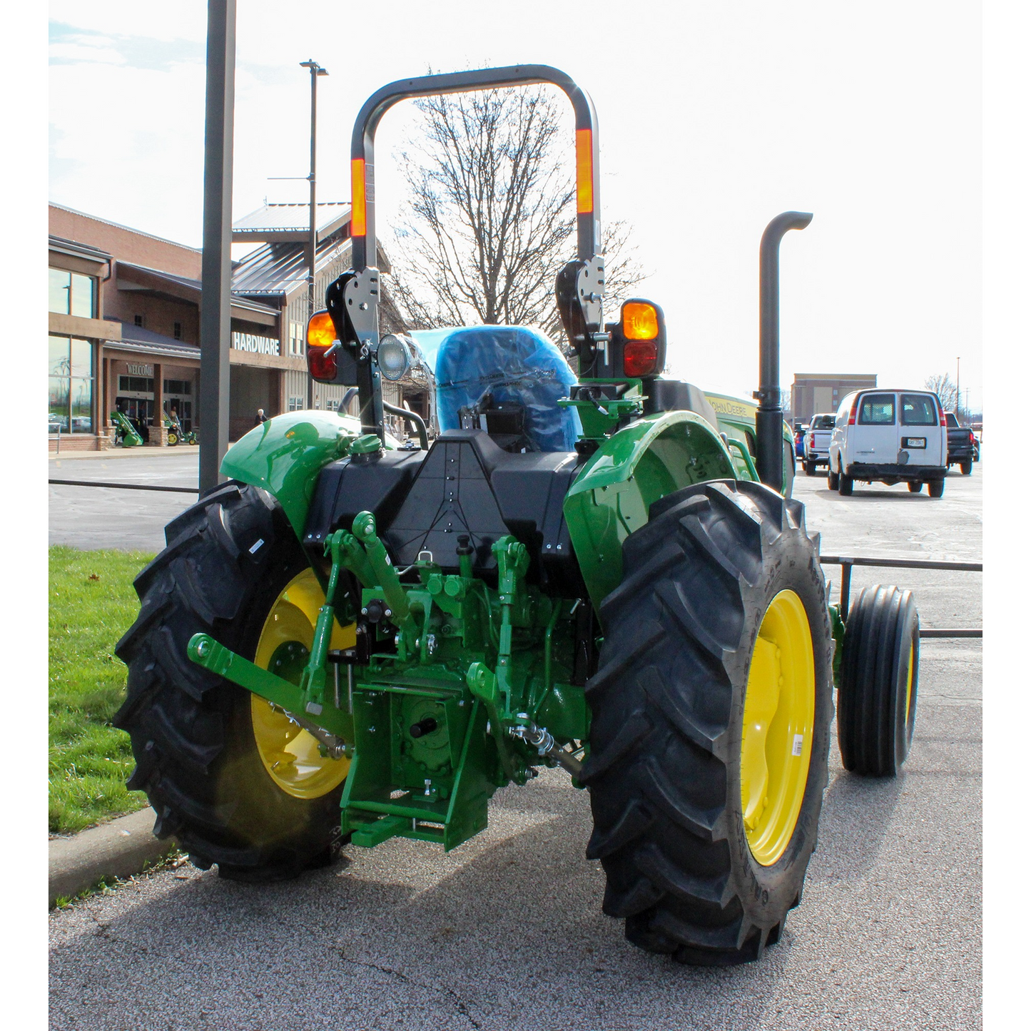 Rear view of a green and yellow John Deere compact utility tractor parked outdoors near a hardware store, part of outdoor power equipment and lawn care tools at Hartville Hardware.