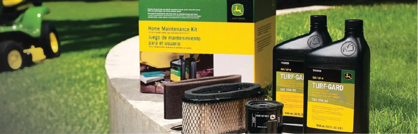 Lawn care maintenance items including oil containers, air and oil filters, and a yellow and green kit box arranged on a curved concrete surface outdoors.