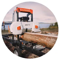 Compact portable sawmill with bright orange accents cutting a large log outdoors near a body of water under a cloudy sky.