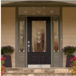 Front entrance of a house featuring a dark wooden door with decorative glass panels, flanked by sidelights and framed by olive green trim, with symmetrical planters on either side.