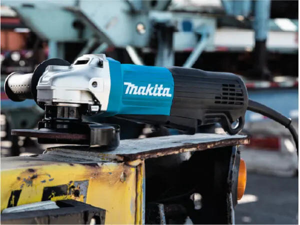 Electric angle grinder with a blue and black housing resting on a worn metal surface in an industrial workshop setting, illustrating a home improvement tool.