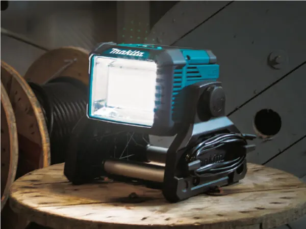 Compact portable work light emitting bright white light, positioned on a wooden spool in a workshop environment.