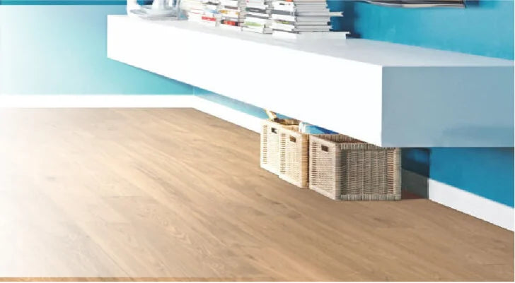 Modern interior scene featuring light wood flooring beneath a floating white shelf with stacked books and wicker baskets against a vibrant blue wall.