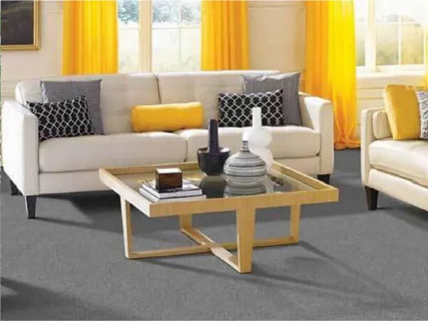 Living room with light gray sofas adorned with patterned and solid yellow cushions, bright yellow curtains, and a wooden coffee table holding decorative items on a gray carpeted floor.