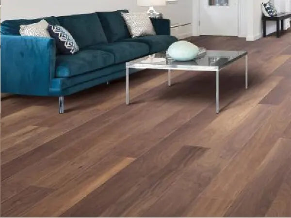 Modern living room with rich wood flooring showcased beneath a teal velvet sofa and a glass coffee table holding decorative items, highlighting home improvement style.