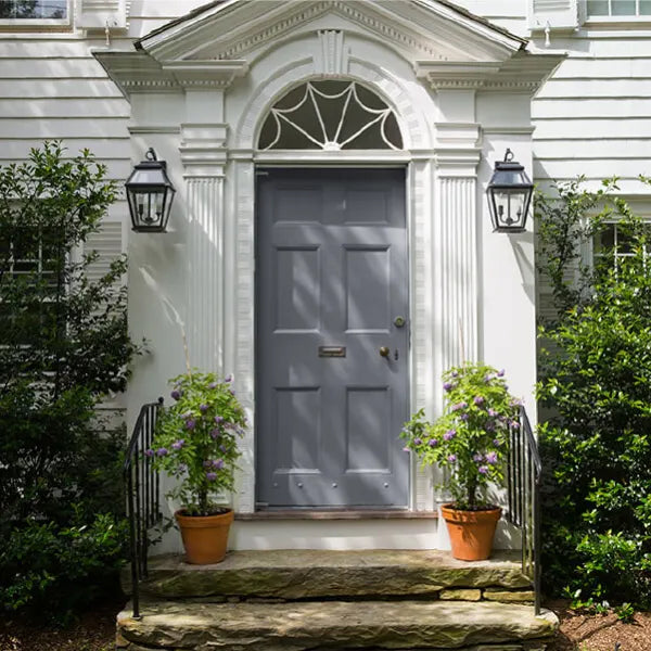 Front entrance with a gray paneled door framed by white classical trim, flanked by black outdoor lanterns and potted plants on stone steps.