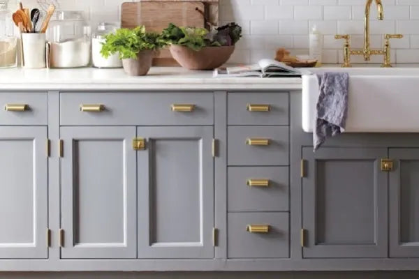 Modern kitchen cabinetry painted in soft gray with brass hardware, white subway tile backsplash, and a white farmhouse sink with a brass faucet.