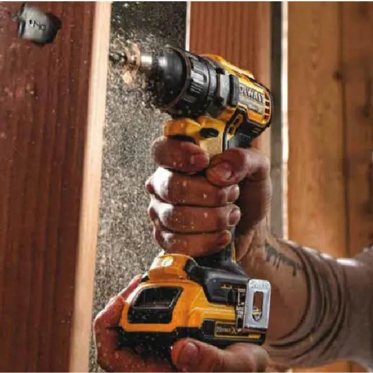 Person's hands holding a yellow and black cordless drill fastening a screw into wooden framing with wood dust particles in the air during construction.