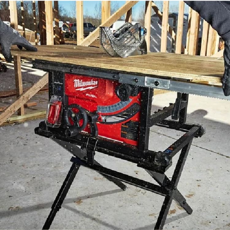 Portable red and black table saw set up outdoors on a concrete surface with lumber being positioned by gloved hands during a wood framing project.