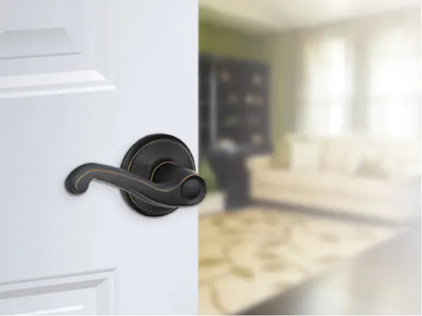 Close-up of a dark metal lever door handle on a partially open white interior door revealing a softly lit living room with a sofa and patterned rug.
