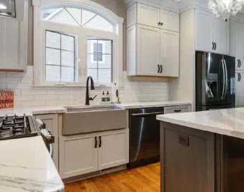 Transitional kitchen featuring neutral cabinetry, a farmhouse sink with black faucet, stainless steel appliances, white subway tile backsplash, and hardwood floors.