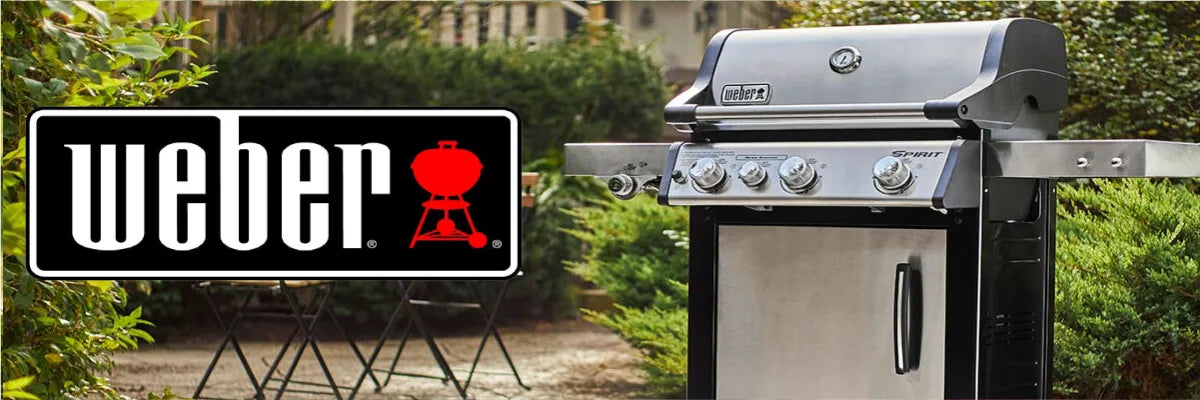 Stainless steel gas grill with four control knobs, side shelves, and a closed cabinet, positioned outdoors on a paved patio with green plants in the background.