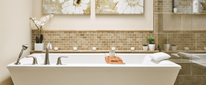 Spacious modern bathroom featuring a white freestanding tub with brushed nickel fixtures, a mosaic tile backsplash, decorative plants, and neutral wall art.