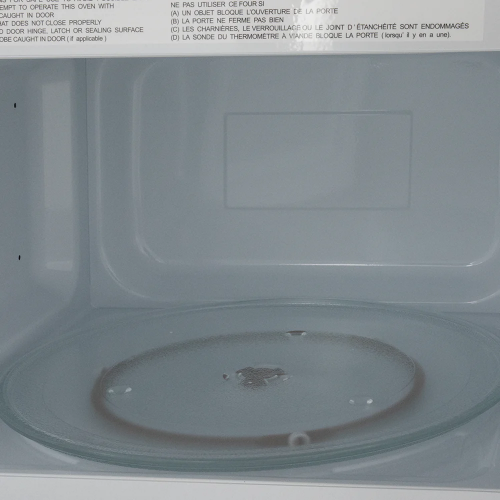 interior view of white microwave oven with glass turntable and warning label for kitchen appliances