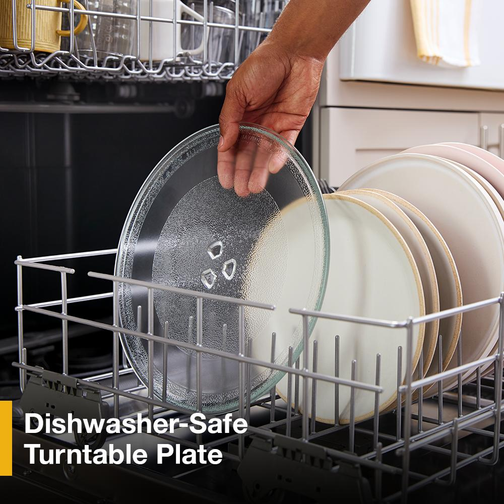 Hand placing a dishwasher-safe glass turntable plate inside a dishwasher with ceramic plates nearby