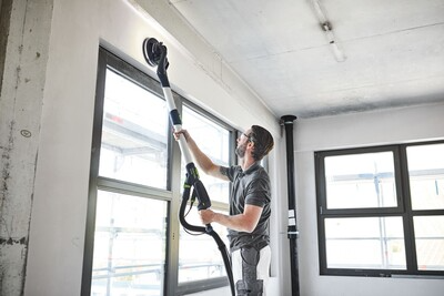 Worker using a power tool with hose clip for ceiling sanding in a home improvement and power tool accessories setting