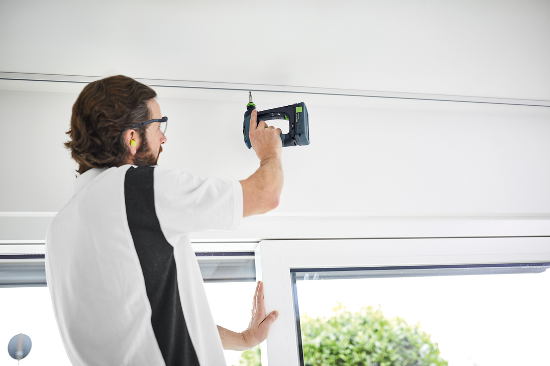 Man using Festool cordless drill to install hardware above window frame for home improvement project