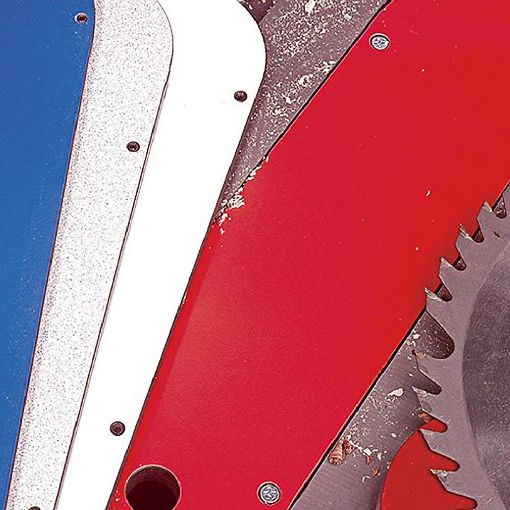 Close-up of colored zero clearance inserts for table saws displayed on a workbench with sawdust and blade edge visible