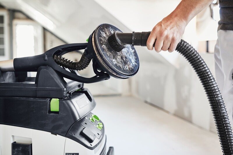 Handheld plastic suction brush attachment connected to vacuum cleaning a dusty interior construction site