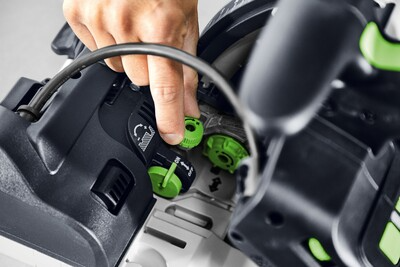 Close-up of person adjusting green dial on Festool plunge cut track saw for precise wood cutting in power tools collection